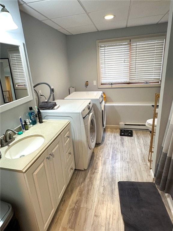 clothes washing area featuring laundry area, light wood finished floors, a baseboard radiator, washing machine and clothes dryer, and a sink