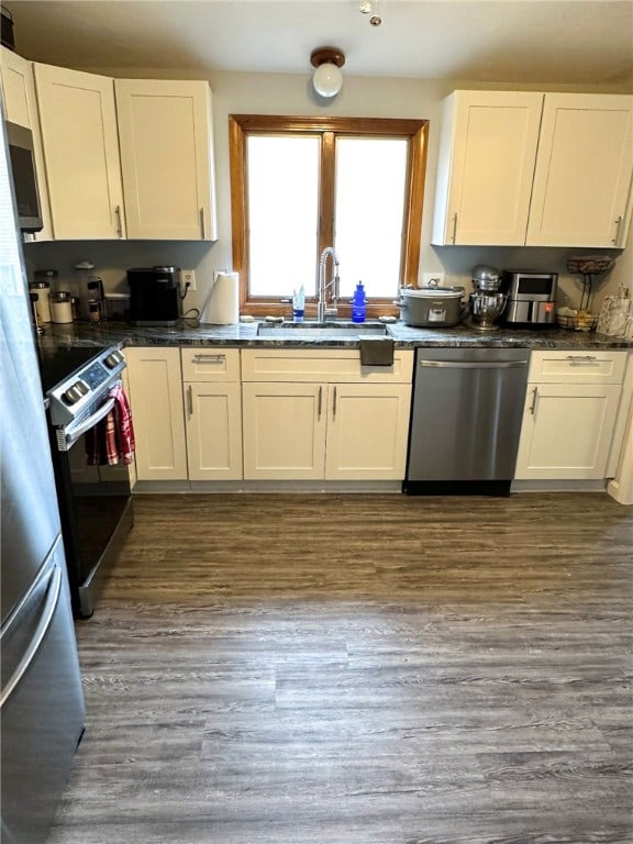 kitchen with dark countertops, stainless steel dishwasher, white cabinetry, a sink, and range with electric stovetop