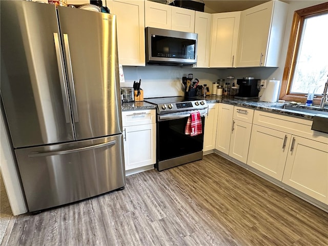 kitchen featuring appliances with stainless steel finishes, light hardwood / wood-style floors, dark stone counters, and white cabinets