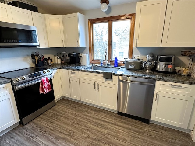 kitchen featuring stainless steel appliances, dark wood-type flooring, a sink, white cabinetry, and dark stone countertops