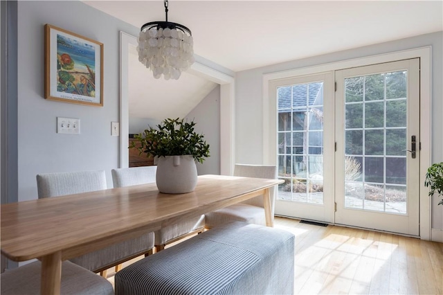 dining space with lofted ceiling, plenty of natural light, a chandelier, and light hardwood / wood-style floors