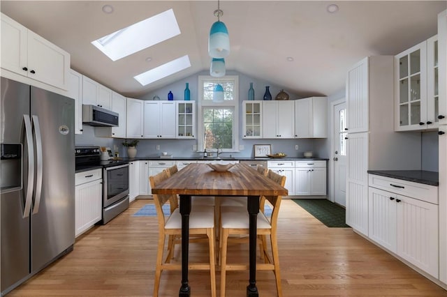 kitchen with appliances with stainless steel finishes, pendant lighting, white cabinets, and light hardwood / wood-style floors