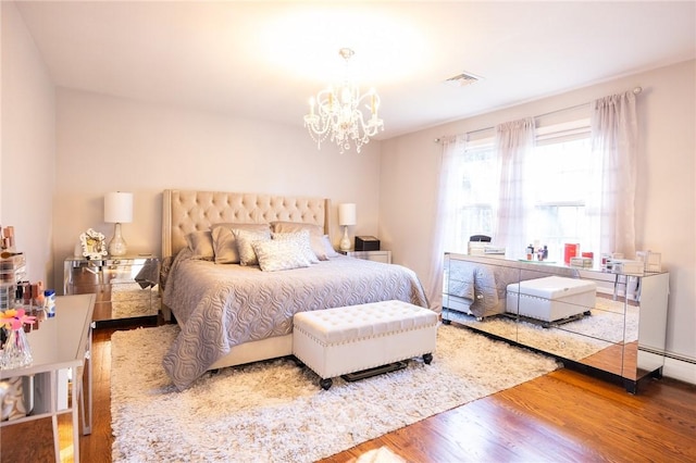 bedroom with an inviting chandelier, hardwood / wood-style floors, and a baseboard heating unit