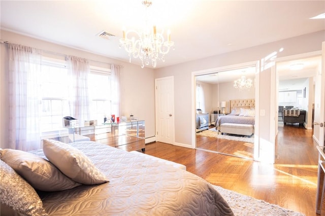 bedroom with a notable chandelier, hardwood / wood-style flooring, a closet, and a baseboard heating unit