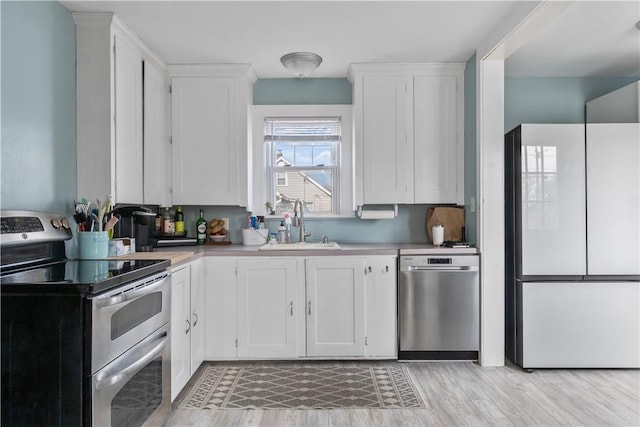 kitchen with light countertops, appliances with stainless steel finishes, a sink, and white cabinets