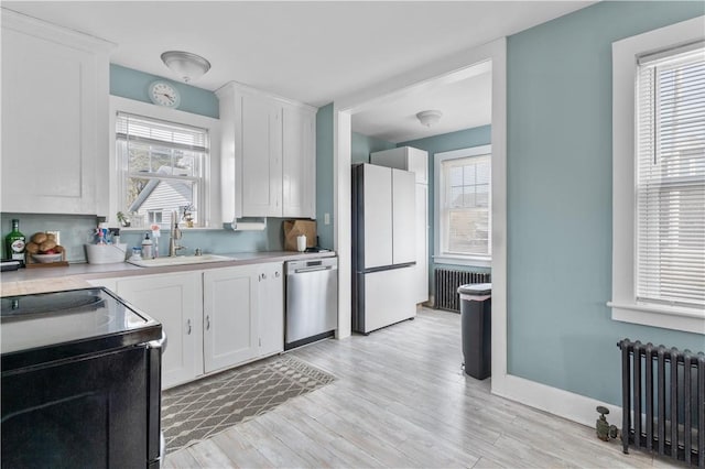 kitchen featuring a sink, white cabinets, freestanding refrigerator, radiator, and dishwasher