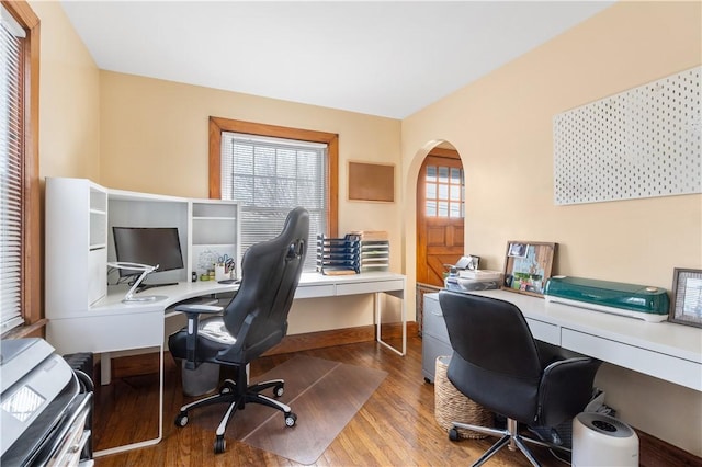 office area with arched walkways, baseboards, and wood finished floors