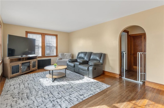 living room with arched walkways, baseboards, hardwood / wood-style flooring, and radiator