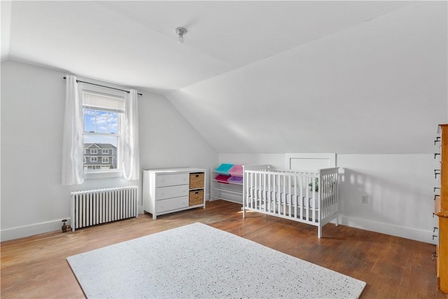 bedroom featuring lofted ceiling, wood-type flooring, radiator, and a crib