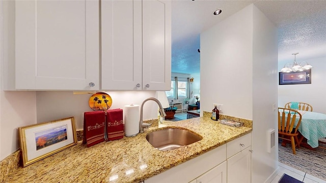 kitchen featuring white cabinetry, sink, a textured ceiling, and light stone counters