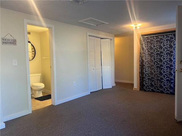 unfurnished bedroom featuring connected bathroom, a textured ceiling, and dark colored carpet