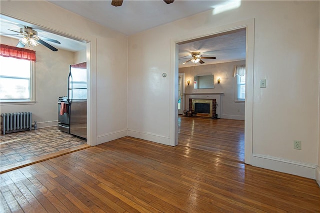 unfurnished room with ceiling fan, dark wood-type flooring, radiator heating unit, and a fireplace