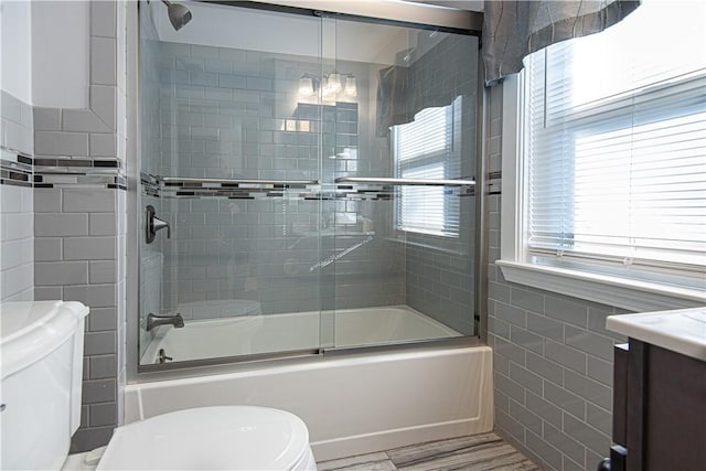 full bathroom with toilet, tile walls, vanity, enclosed tub / shower combo, and hardwood / wood-style floors