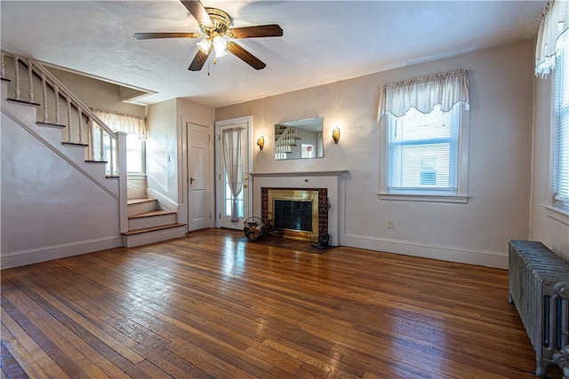 unfurnished living room with ceiling fan, a brick fireplace, radiator heating unit, and dark hardwood / wood-style flooring