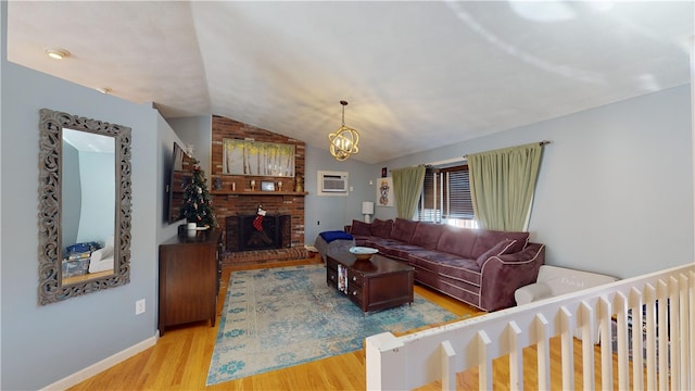 living area with a wall unit AC, vaulted ceiling, light wood-style floors, a fireplace, and a chandelier