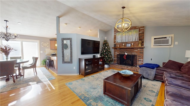 living room featuring a chandelier, light wood finished floors, vaulted ceiling, and a wall unit AC