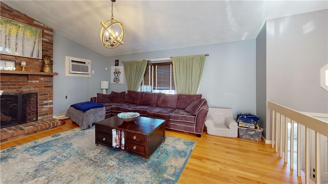 living room featuring light wood finished floors, a wall unit AC, an inviting chandelier, vaulted ceiling, and a fireplace