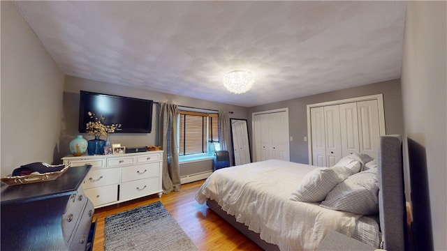 bedroom featuring light wood finished floors, baseboard heating, and two closets