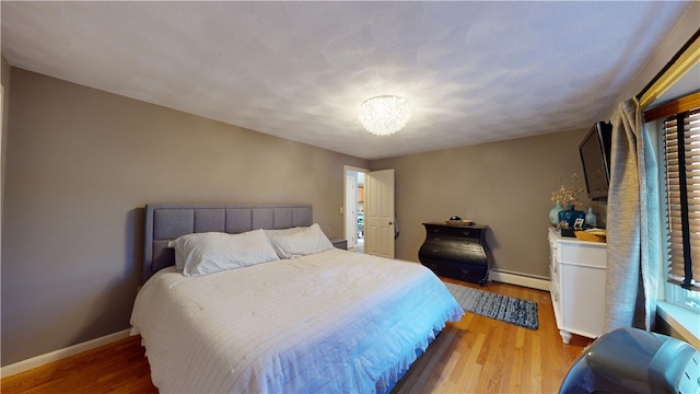 bedroom with a baseboard radiator, baseboards, and wood finished floors