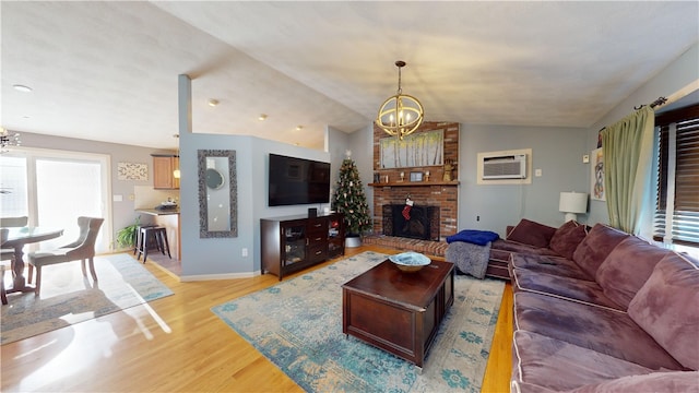 living area with lofted ceiling, a wall unit AC, light wood-style flooring, a brick fireplace, and an inviting chandelier