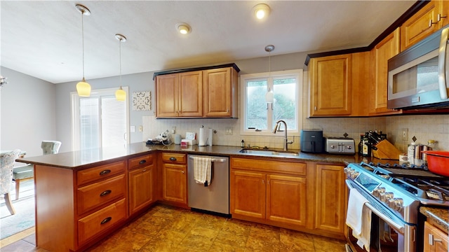 kitchen featuring stainless steel appliances, dark countertops, a sink, and decorative light fixtures