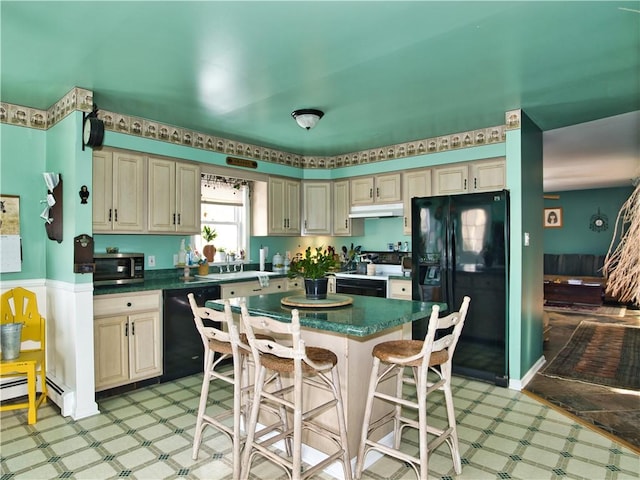 kitchen featuring a breakfast bar, a center island, baseboard heating, black appliances, and cream cabinets