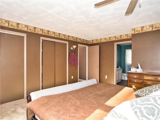 bedroom featuring ensuite bathroom, a textured ceiling, multiple closets, carpet flooring, and ceiling fan