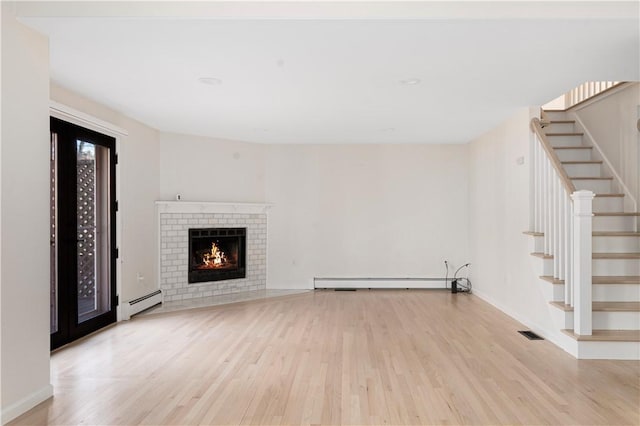 unfurnished living room featuring a brick fireplace, a baseboard heating unit, and light wood-type flooring