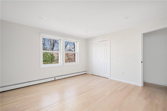 unfurnished bedroom with baseboard heating, light hardwood / wood-style floors, and a closet