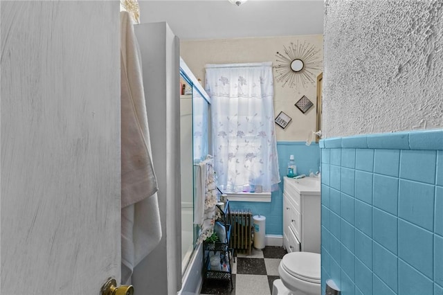 full bathroom with bath / shower combo with glass door, radiator heating unit, tile walls, vanity, and toilet