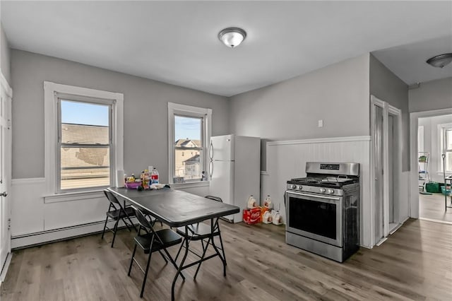 kitchen featuring white refrigerator, hardwood / wood-style floors, a baseboard heating unit, and stainless steel range with gas stovetop