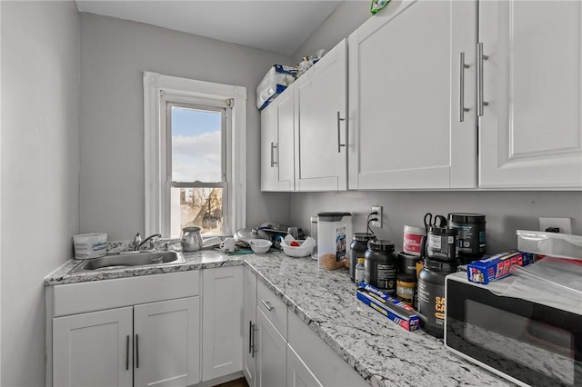 kitchen with white cabinetry, sink, and light stone counters