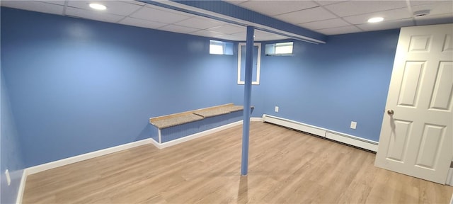 basement featuring a baseboard radiator, light hardwood / wood-style floors, and a drop ceiling