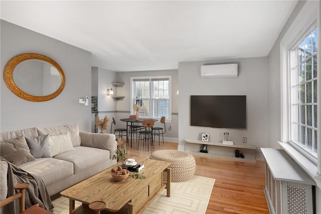 living room featuring light hardwood / wood-style floors, an AC wall unit, and a healthy amount of sunlight