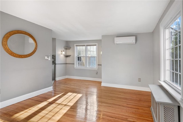 unfurnished room with plenty of natural light, a wall mounted air conditioner, and light hardwood / wood-style flooring