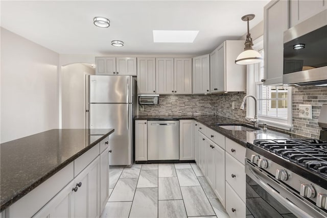 kitchen with sink, hanging light fixtures, appliances with stainless steel finishes, dark stone counters, and backsplash