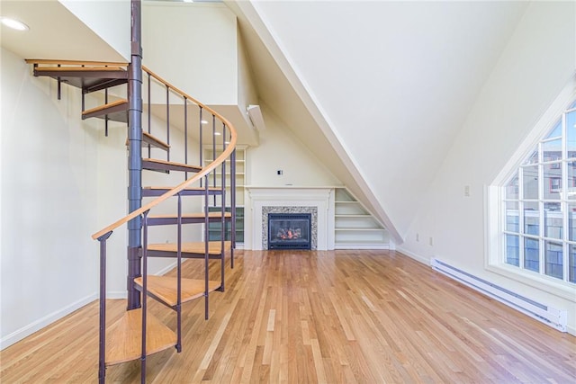 unfurnished living room with light hardwood / wood-style flooring, a tiled fireplace, plenty of natural light, and baseboard heating