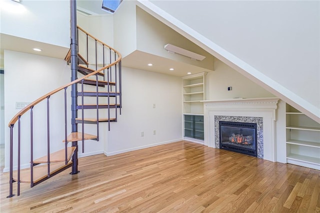 unfurnished living room with built in shelves, light hardwood / wood-style flooring, a high end fireplace, and a high ceiling