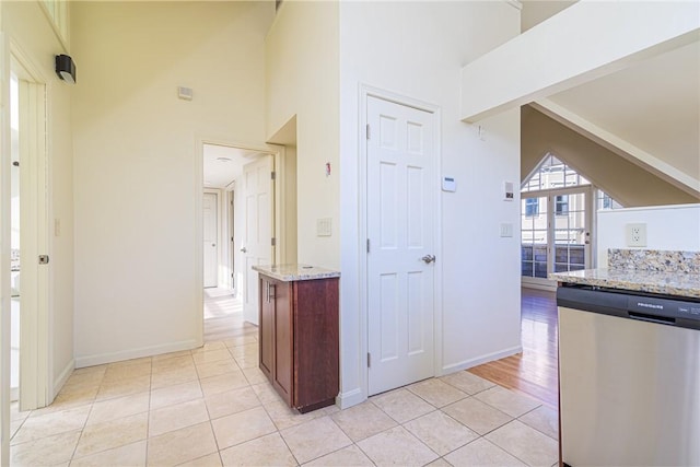 kitchen featuring light stone countertops, stainless steel dishwasher, high vaulted ceiling, and light tile patterned floors