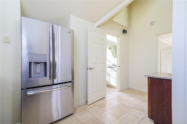 kitchen with light stone counters, stainless steel fridge, vaulted ceiling, and light tile patterned floors