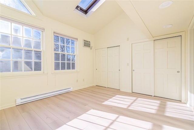 unfurnished bedroom with a skylight, multiple closets, a wall unit AC, light hardwood / wood-style floors, and a baseboard heating unit