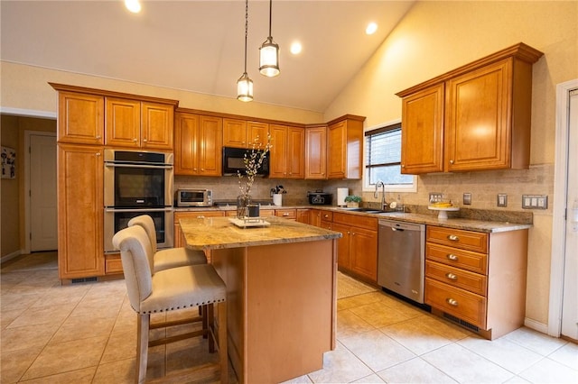 kitchen featuring sink, light stone counters, decorative light fixtures, a kitchen island, and stainless steel appliances