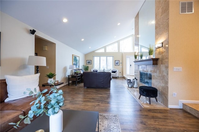 living room with dark hardwood / wood-style floors, a tiled fireplace, and high vaulted ceiling