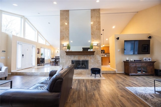 living room featuring wood-type flooring, a tiled fireplace, and high vaulted ceiling