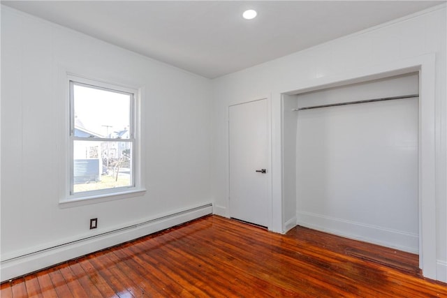 unfurnished bedroom featuring dark wood-type flooring, a closet, and baseboard heating