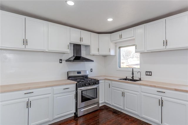 kitchen with wood counters, stainless steel gas stove, white cabinetry, sink, and wall chimney exhaust hood