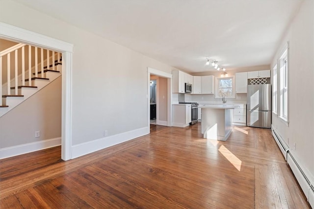 kitchen with a kitchen island, white cabinets, hardwood / wood-style flooring, baseboard heating, and stainless steel appliances