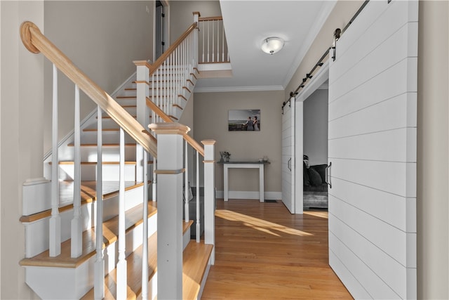 staircase with wood-type flooring, ornamental molding, and a barn door