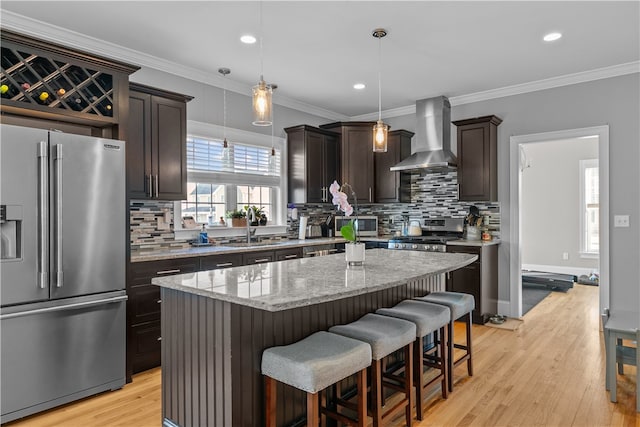 kitchen featuring light stone counters, a center island, hanging light fixtures, stainless steel appliances, and wall chimney range hood