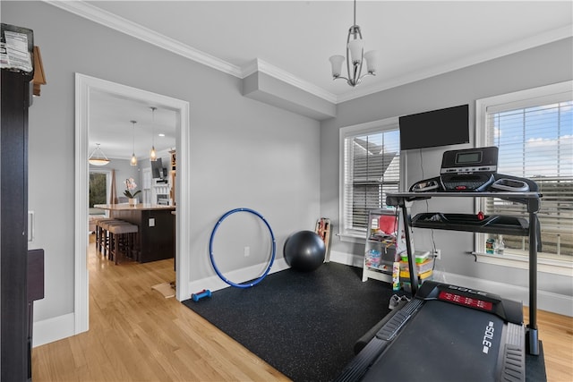 exercise room featuring a notable chandelier, ornamental molding, and light wood-type flooring